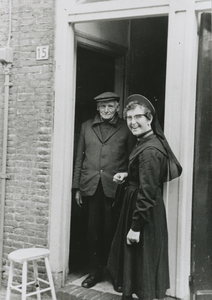 876924 Afbeelding van een Zuster Augustines die een praatje maakt met een oudere man, die in de deuropening staat van ...